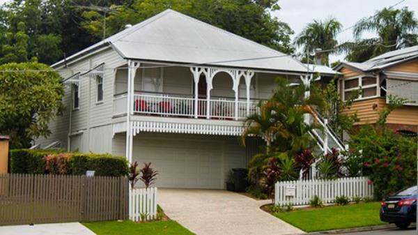 White queenslander home with tropical greenery and tall trees on overcast day in Australia.