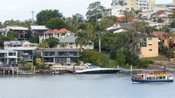 The Brisbane River Tour Guide Boat with tourist cruising along the Australian Brisbane River. Expensive riverside properties in the background.