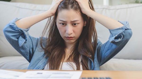 Young woman with hands on head appears stressed a<em></em>bout her mortgage statement.
