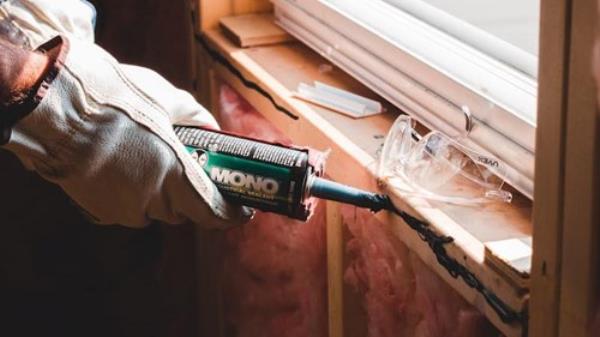 Glue gun being applied by gloved hand to window sill of house under renovation