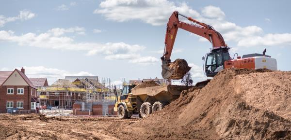 A picture of a construction development for new homes, with a crane and a dump truck in view on dirt lots.
