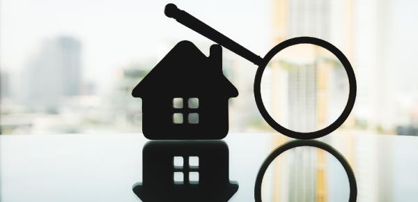 A silhouetted picture of a house miniature and a magnifying glass resting along it.