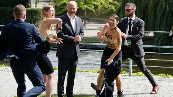 Two activists standing next to German Chancellor Olaf Scholz protest for a gas embargo during the 'open doors' event at the chancellery in Berlin