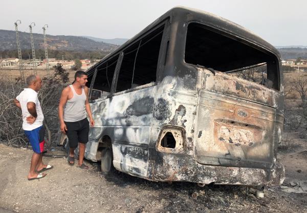 Men inspect a bus that was burnt following a wildfire in El Kala