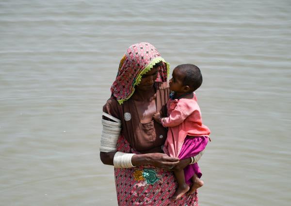 A woman carries her baby as she walks through rain waters following rains and floods during the monsoon season in Jamshoro