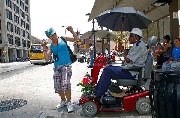 Fowler shields himself from the sun as he waits to board a bus during a prolonged heat wave in Dallas, Texas