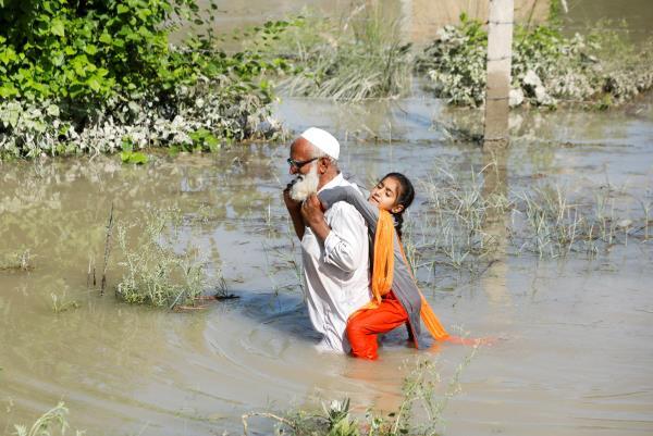 A man wades through flood waters carrying his grand daughter on his back following rains and floods during the monsoon season in Charsadda