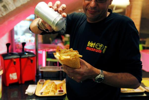 A cook sprinkles salt on fries at a cafe in the Frietmuseum in Bruges