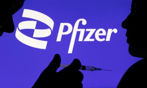 People pose with syringe with needle in front of displayed Pfizer logo