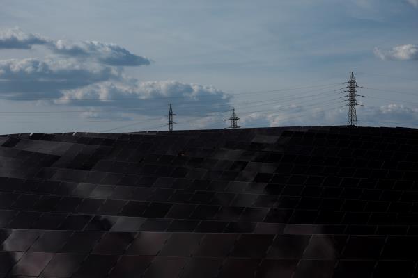 High-voltage power lines and electricity pylons stand near an array of solar panels from a solar energy park in Saelices