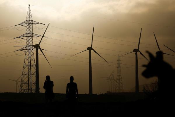 Two people walk near an electricity pylon and a group of wind turbines, in Barranco de Tirajana