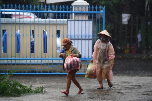 Two women in plastic overcoats and carrying bags walk outside in the rain in Hoi An, Vietnam.