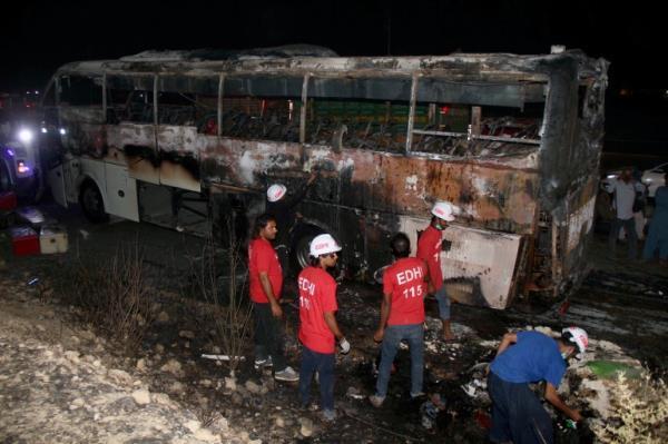 Volunteers gather beside a charred bus on a highway, in Nooriabad, Pakistan, Thursday, Oct. 13, 2022. Police say the bus fire killed over a dozen flood survivors, including children and two women. (AP Photo/Pervez Masih)