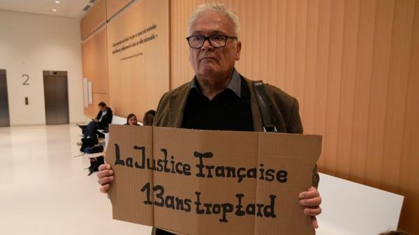 A man holds a placard reading 'The French justice, 13 years too late' prior to the start of the trial. Pic: AP