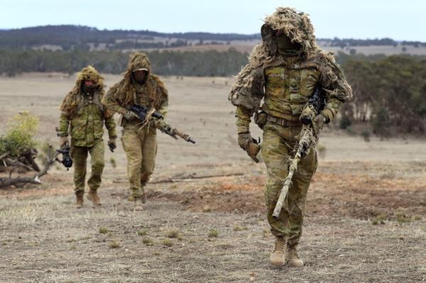 Three men in army uniform on an open, dirt area