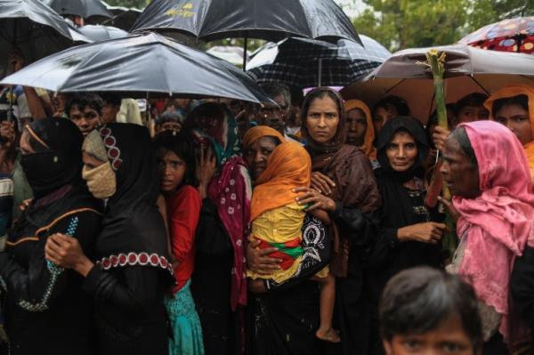 Rohingya refugee women with their children stand in a queue outside a food distribution center at Balukhali refugee camp