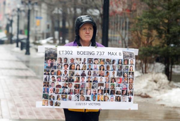 Moore wearing a helmet is standing in the street, holding a poster showing the faces of the victims of the crash