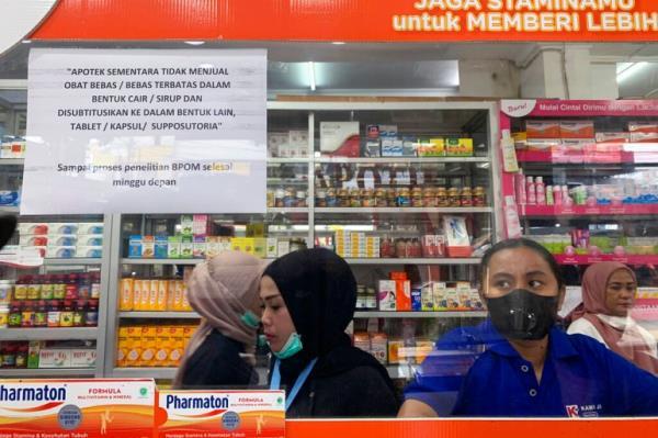 Pharmacy employees in Jakarta, Indonesia, wait for customers at a counter displaying a notification saying that the sale of medicinal syrup is temporarily halted on October 20, 2022 
