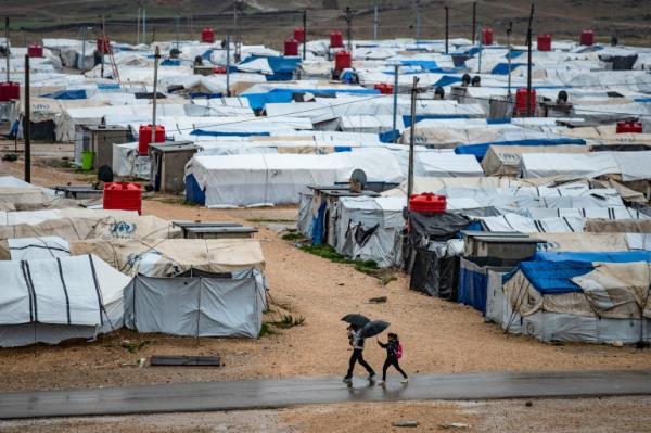 People use umbrellas as they walk in the rain at Camp Roj, where relatives of people suspected of belonging to ISIL (ISIS) are held in Syria's northeastern Hasakah province 