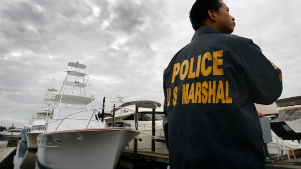 Roland Ubaldo of the U.S. Marshal's office keeps watch near a vintage Rybovich M/V "The Bull" sportfish yacht (L), owned by Bernard Madoff, in the dockyard at the National Liquidators in Davie, Florida November 16, 2009. The 55-footer is among three Madoff vessels up for sale in a live auction tomorrow with proceeds going to victim restitution. REUTERS/Hans Deryk (UNITED STATES CRIME LAW BUSINESS SOCIETY SPORT YACHTING)