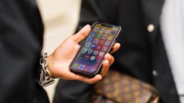 A guest wears silver bracelet, holds in his hand an iPhone unlocked on the application screen, outside Officine G��n��rale, during Paris Fashion Week - Menswear Spring/Summer 2022, on June 25, 2021 in Paris, France.