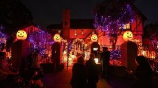 TOPSHOT - People look at a home decorated with pumpkins and ghosts for Halloween, in Burbank, California, October 30, 2021. - Last year's Halloween celebrations were severely curtailed due to the Covid-19 pandemic. (Photo by Robyn Beck / AFP) (Photo by ROBYN BECK/AFP via Getty Images)