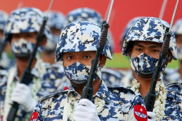Close up of several men in camouflage gear holding up rifles with attached bayonets.