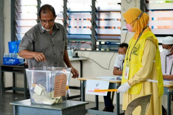 A voter puts his ballot in the box in a polling station set up in a classroom as an alection officials wearing yellow watches