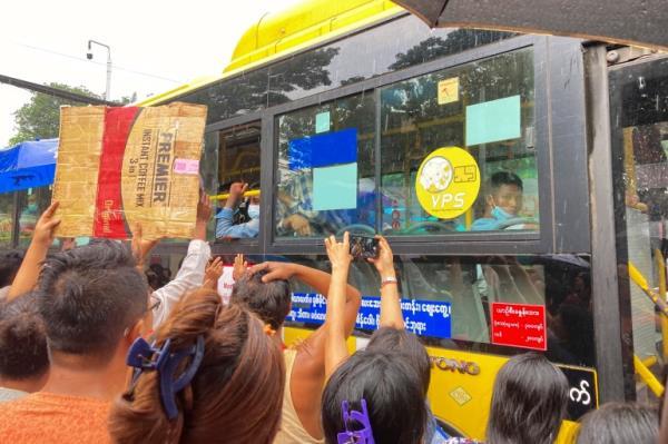 People stretching to reach the window of a bus, holding signs with names, as they hope their loved ones are released from prison