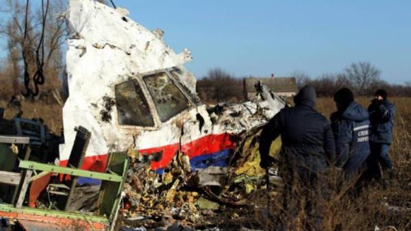 Two workers coming up to front of plane wreck (white with red and blue stripe at bottom) surrounded by debris