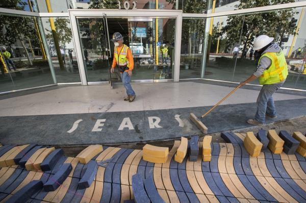 Cesar Villasenor, right, sweeps away dirt around the original Sears logo located in front of the main entrance on Colorado Ave. to the vacant Sears store in Santa Monica that has recently undergone a $50 million makeover to turn the Art Deco-style building into an office, restaurant and retail complex. In foreground are new wave design concrete pavers to match the existing design on Colorado Ave. 