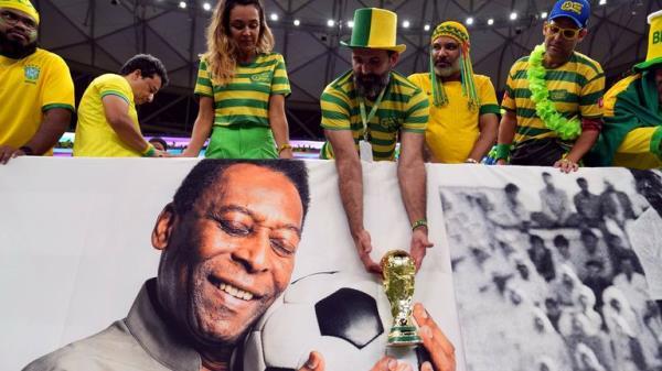 A Brazil fan holds a replica World Cup trophy over a picture of former player Pele ahead of the FIFA World Cup Group G match at the Lusail Stadium in Lusail, Qatar. Picture date: Friday December 2, 2022.
