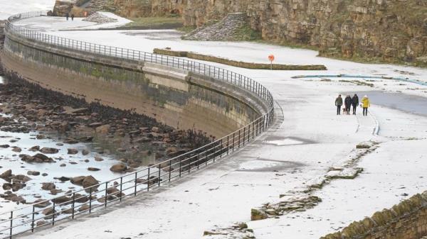 People walk along the seafront at Whitley Bay in Northumberland after a light covering of snow. Snow and ice have swept across parts of the UK, with cold wintry conditions set to continue for days. Picture date: Sunday December 11, 2022.