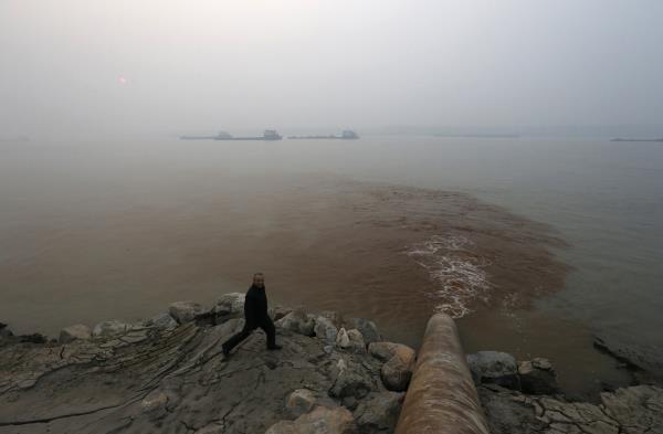 A man walks by a pipe discharging waste water into the Yangtze River from a paper mill in Anqing