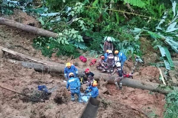 A rescue team searches for survivors in the mud after a landslide in Malaysia. They are working close to fallen trees