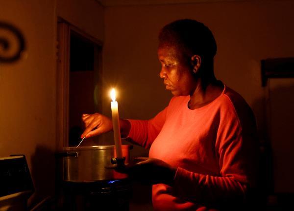 Maria Modiba cooks by a candlelight during a power outages in Soweto